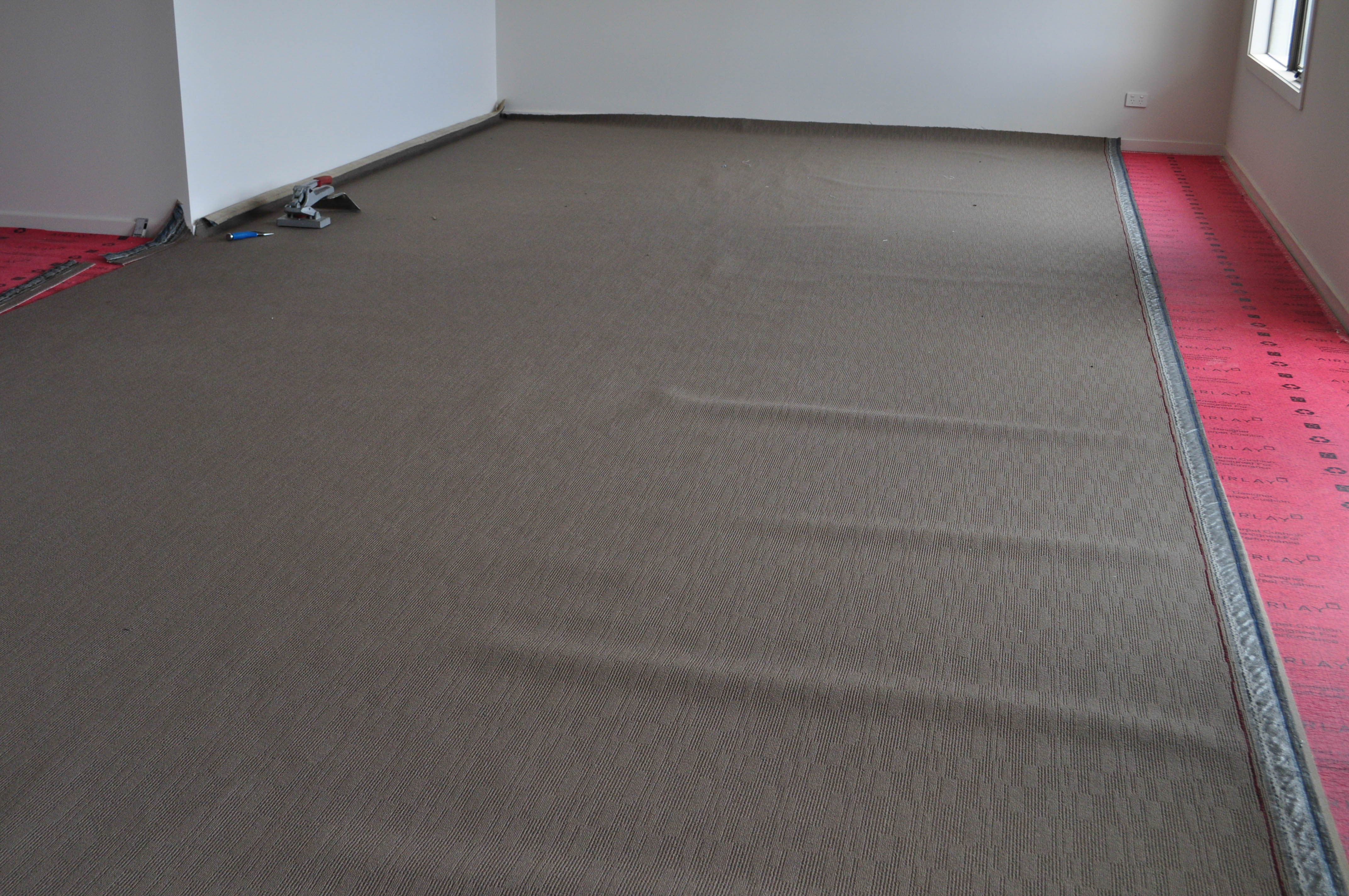 carpet laying process under way by Concord Floors, showing a roll of carpet stretched out, on top of installed red underlay in a home in
 Point Cook, Werribee.