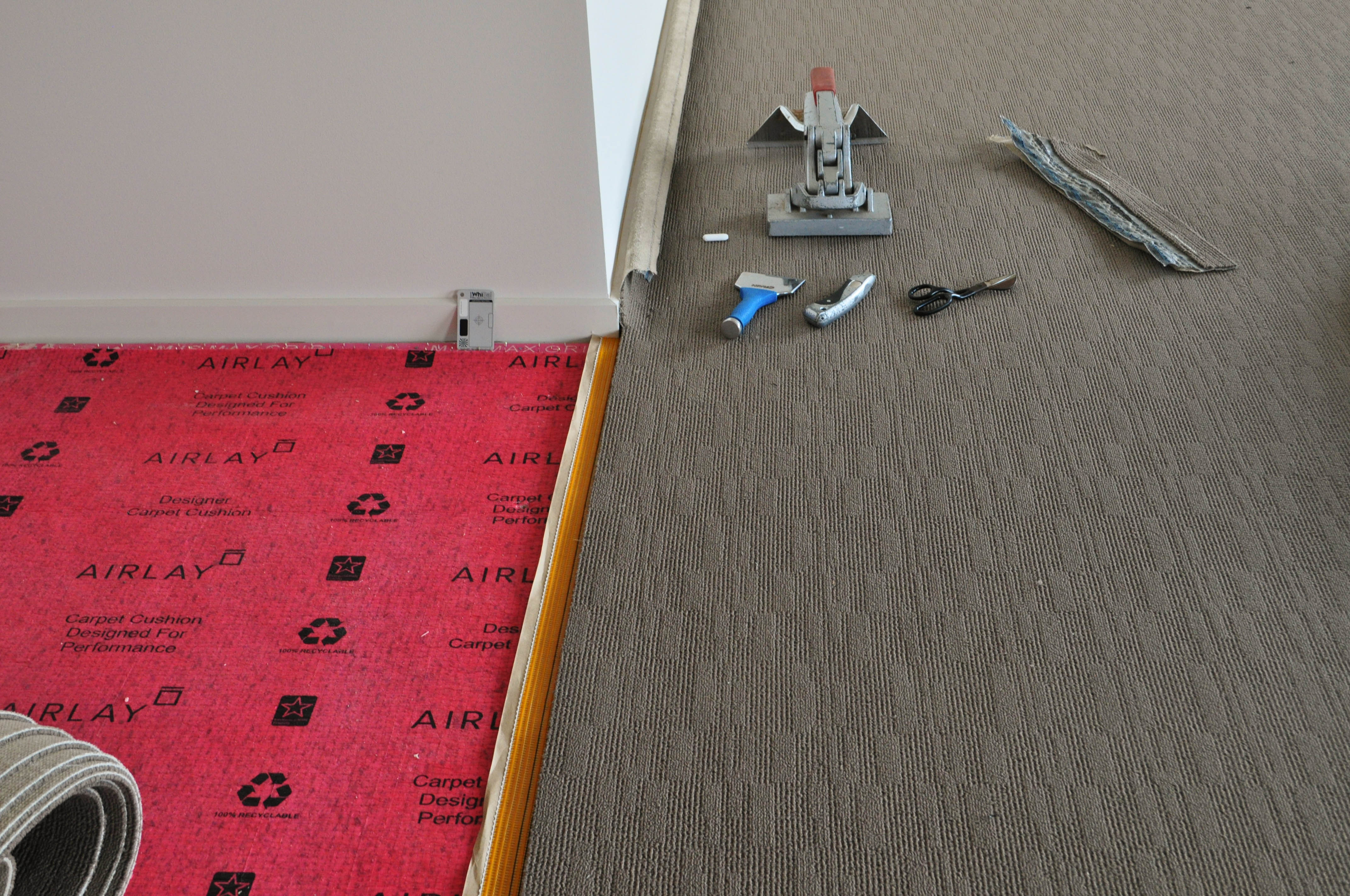 carpet laying process under way by Concord Floors, showing a roll of carpet stretched out and prepared for joining to other carpet roll
 , on top of installed red underlay in a home in Point Cook, Werribee.