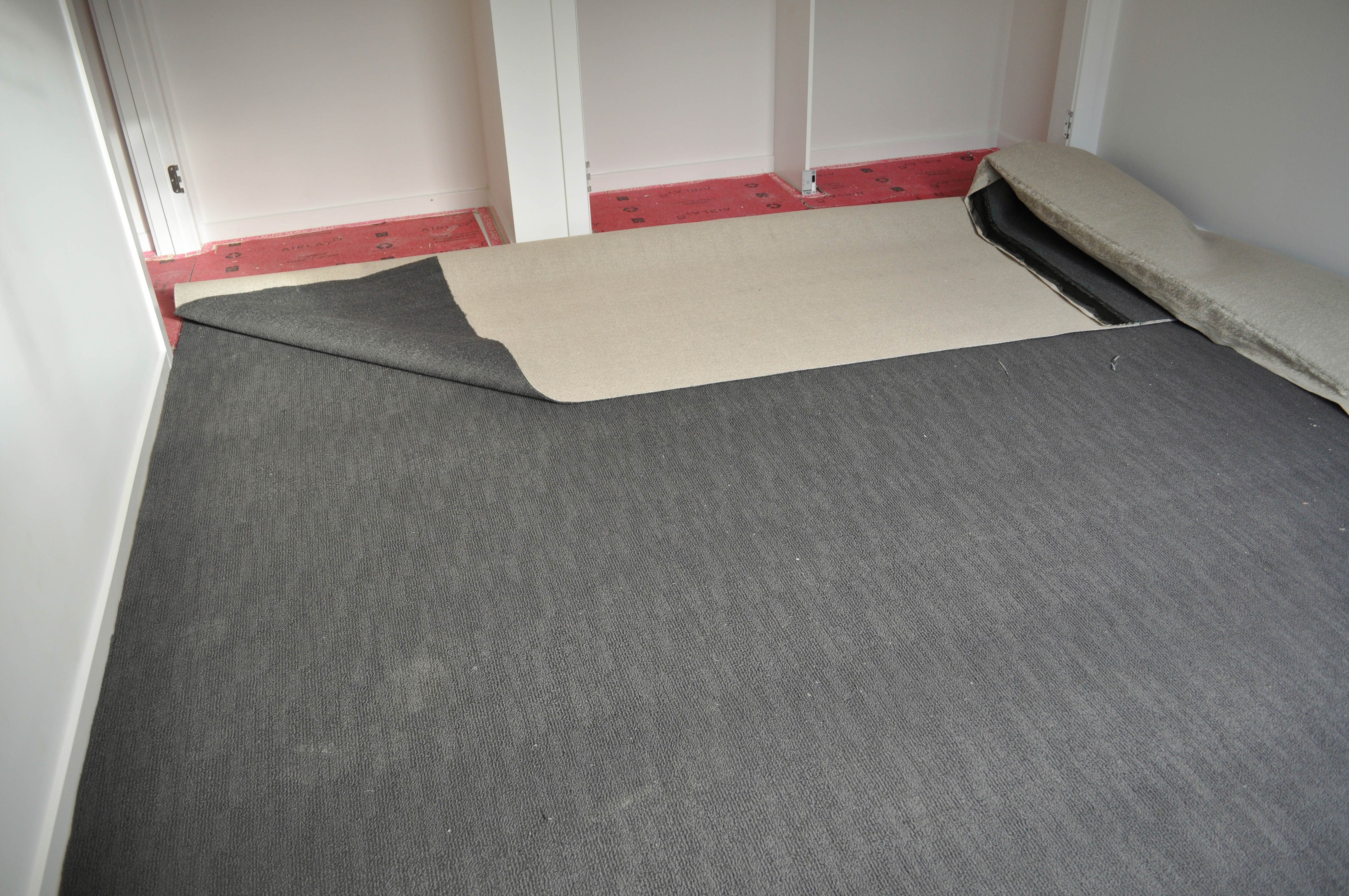 carpet laying process under way by Concord Floors, showing a roll of carpet stretched out, on top of installed red underlay in a home in
 Werribee.