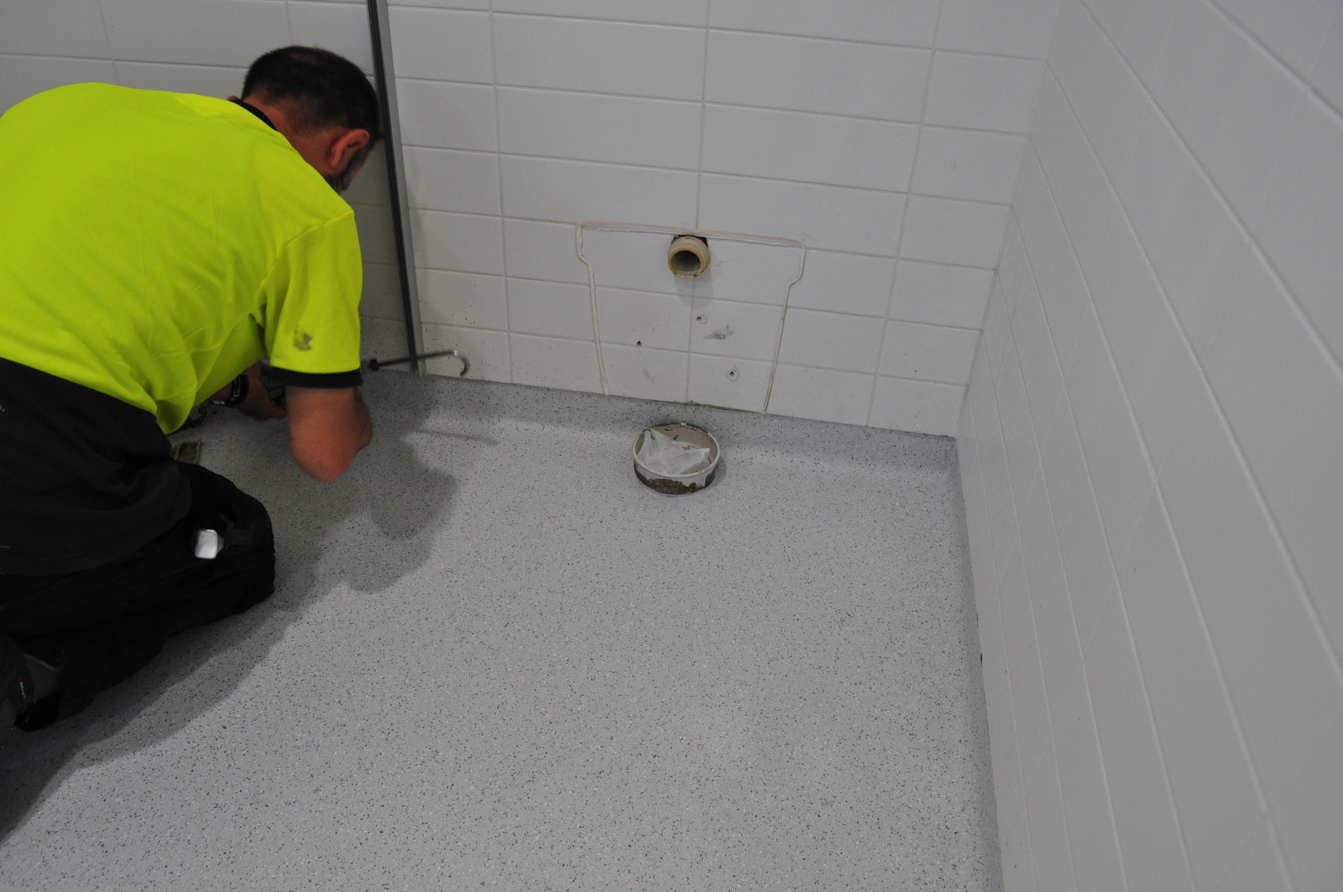showing the floor of a corner of the toilet in which the floor has been covered by vinyl and the vinyl installer is finishing off the coving.